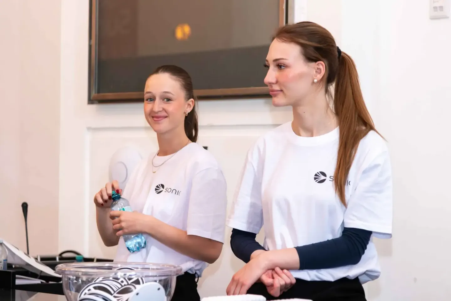 Zwei Moderatorinnen in weißen Sonic-Shirts präsentieren beim Sonic Summit Event in Wien, eine hält eine Wasserflasche