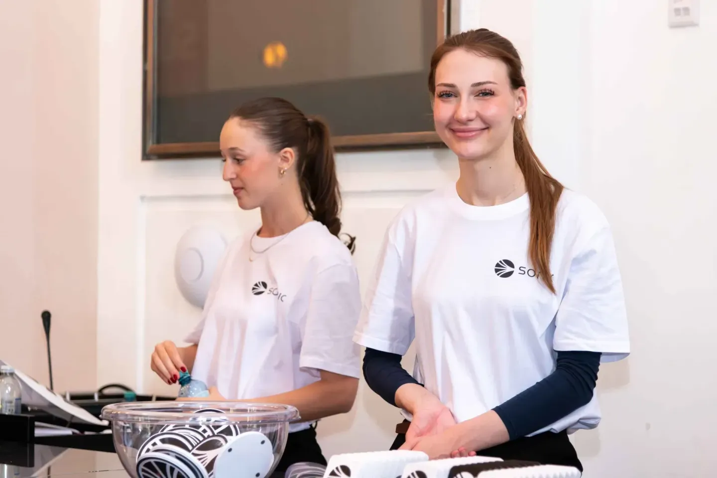 Zwei junge Frauen in weißen Sonic-Summit-T-Shirts präsentieren ein Projekt bei einem Firmenevent Wien