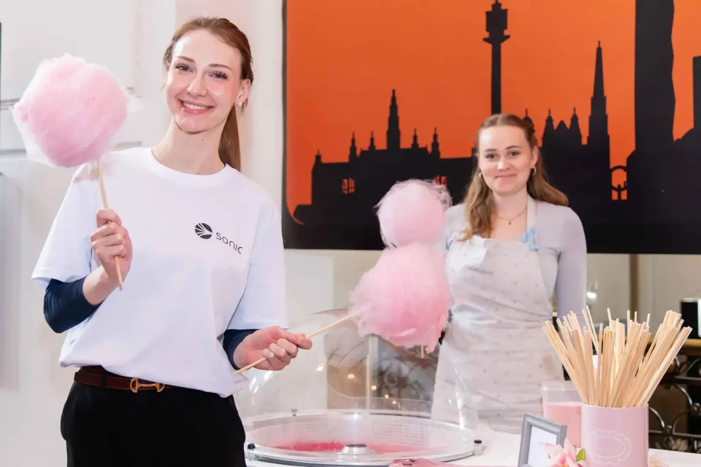 Zwei junge Frauen mit rosafarbener Zuckerwatte auf dem Sonic Summit Event in Wien, im Hintergrund eine Skyline-Silhouette