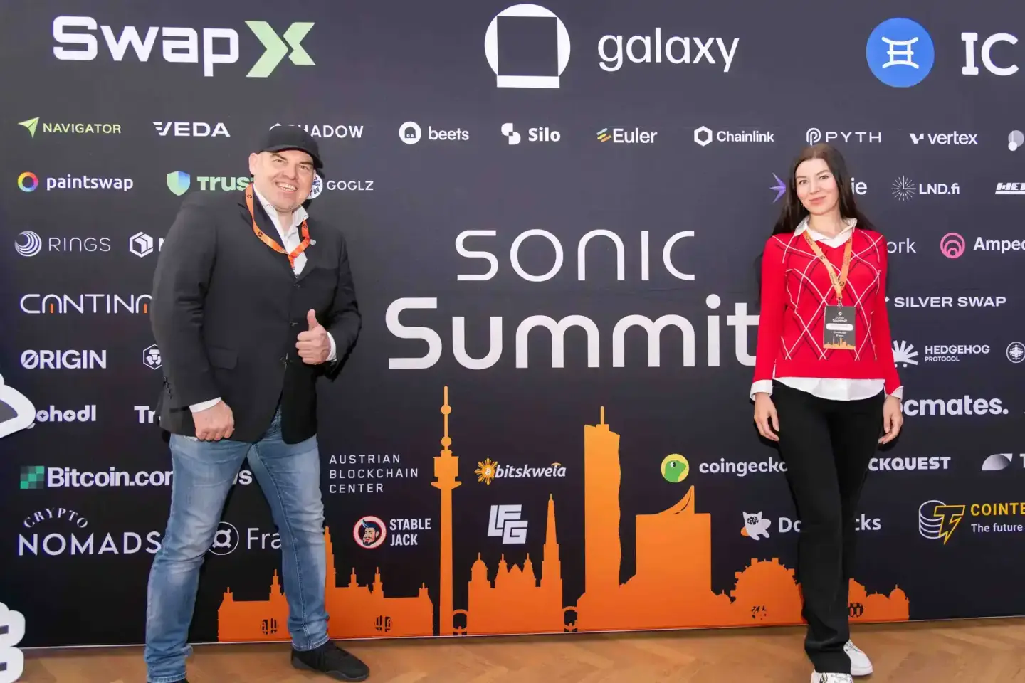 Zwei Personen posieren vor der Sonic Summit Bühne in Wien mit Stadtsilhouette und Sponsor-Logos als Eventfotografie