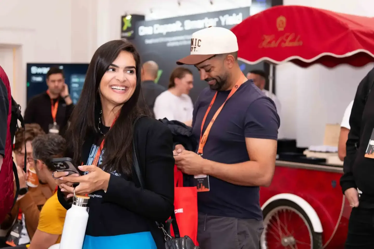 Zwei Personen mit Lanyards beim Sonic Summit Event in Wien, eine Frau mit schwarzem Blazer und ein Mann mit Kappe unterhalten