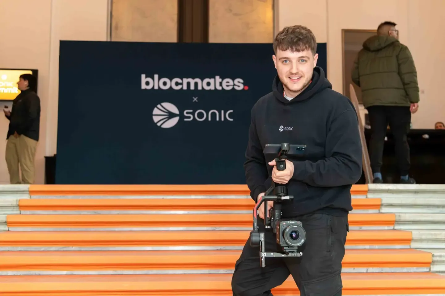 Eventfotograf hält professionelle Kamera vor Blocmates x Sonic Bühne mit orangenen Stufen