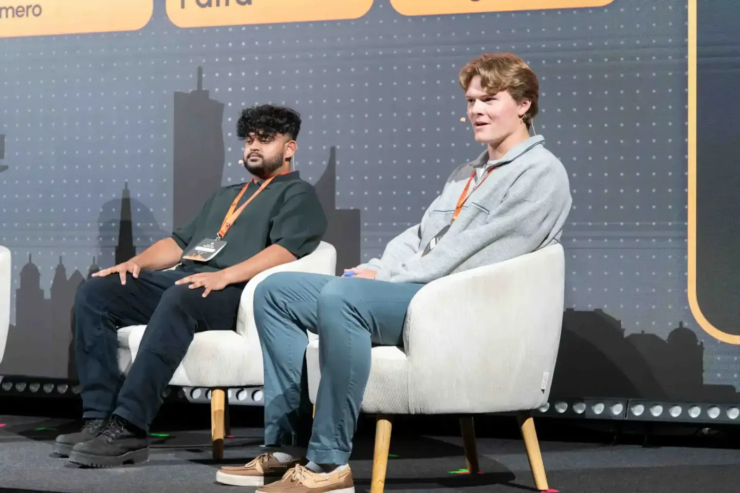 Zwei Sprecher sitzen auf weißen Sesseln bei einer Podiumsdiskussion auf der Sonic Summit Konferenz, im Hintergrund eine Skyli