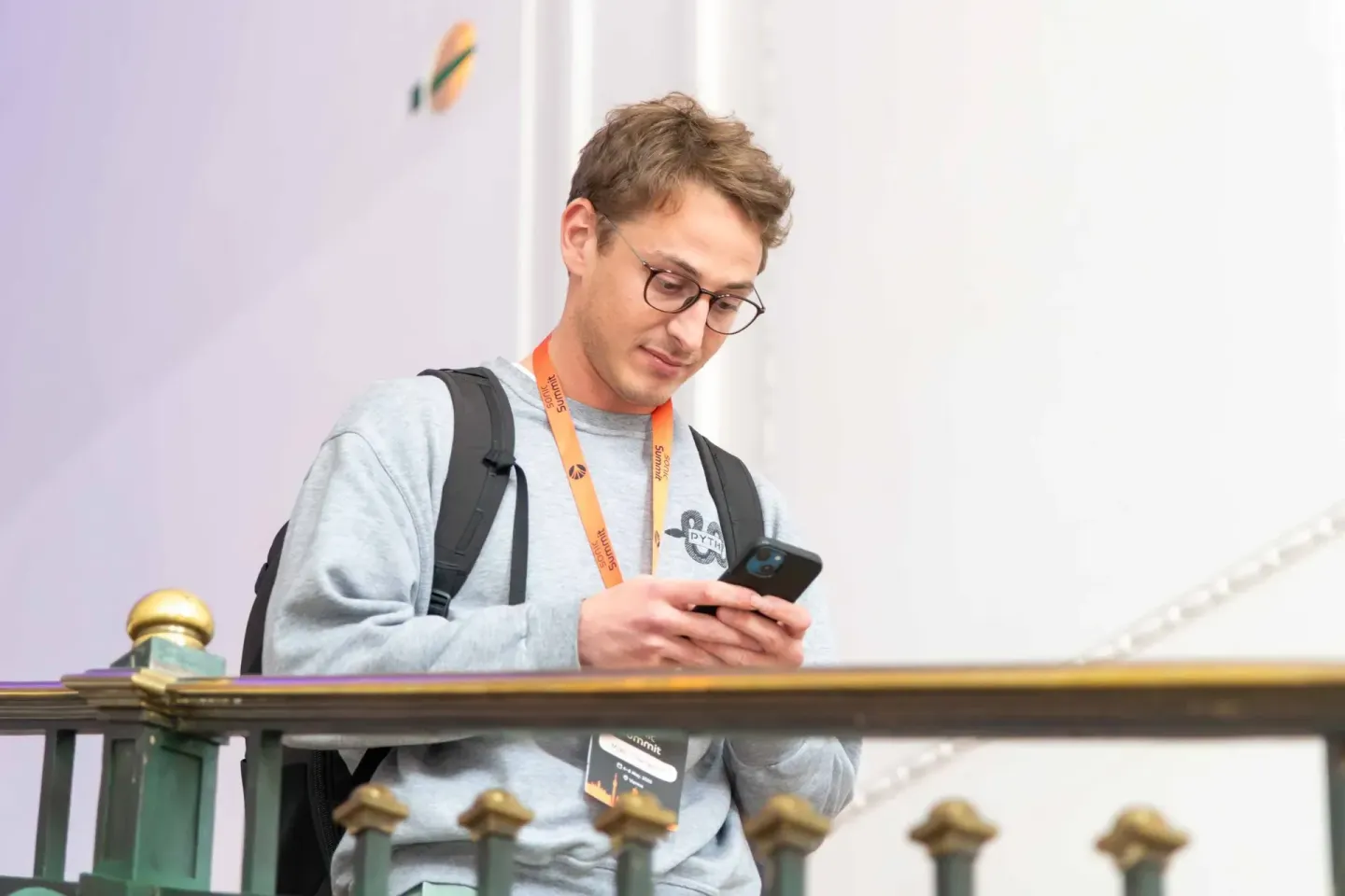 Junger Mann mit Brille schaut auf sein Smartphone an einem Geländer während eines Events – Eventfotografie Wien