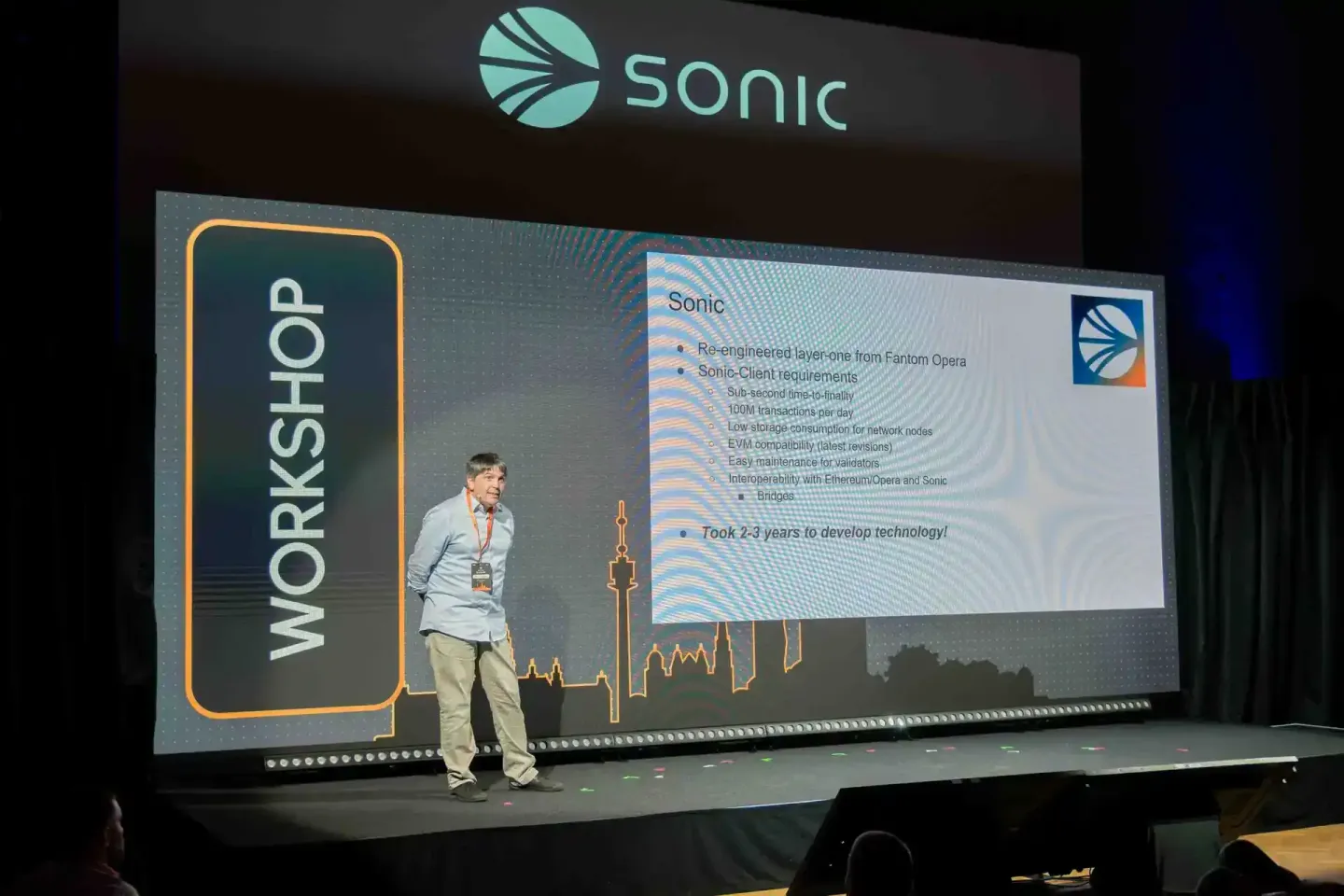 Sprecher präsentiert Sonic-Technologie auf der Bühne beim Sonic Summit Wien vor großem Screen mit Veranstaltungsfotograf