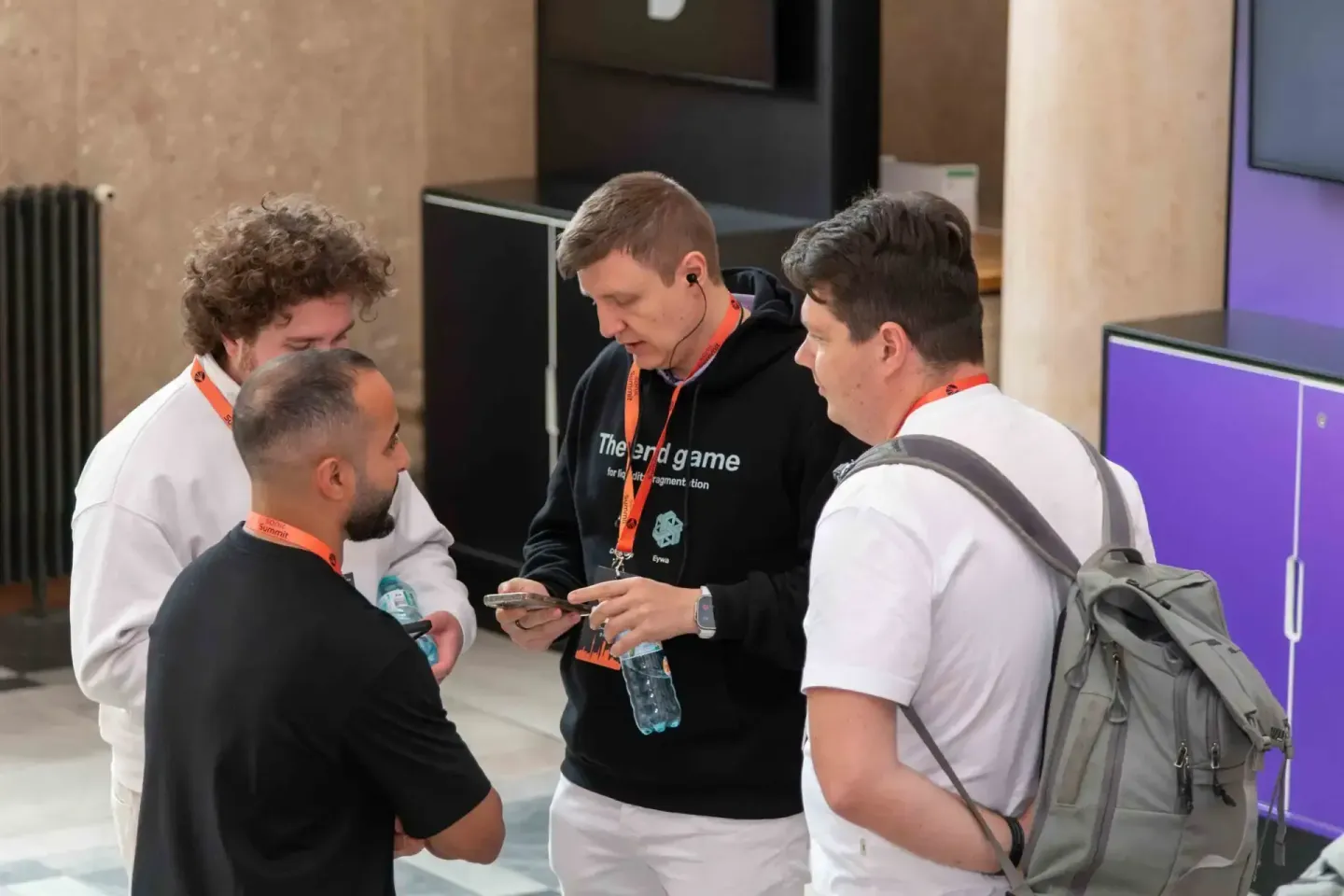 Vier Personen mit orange Lanyards diskutieren beim Sonic Summit Event in Wien, Eventfotograf dokumentiert Networking-Moment