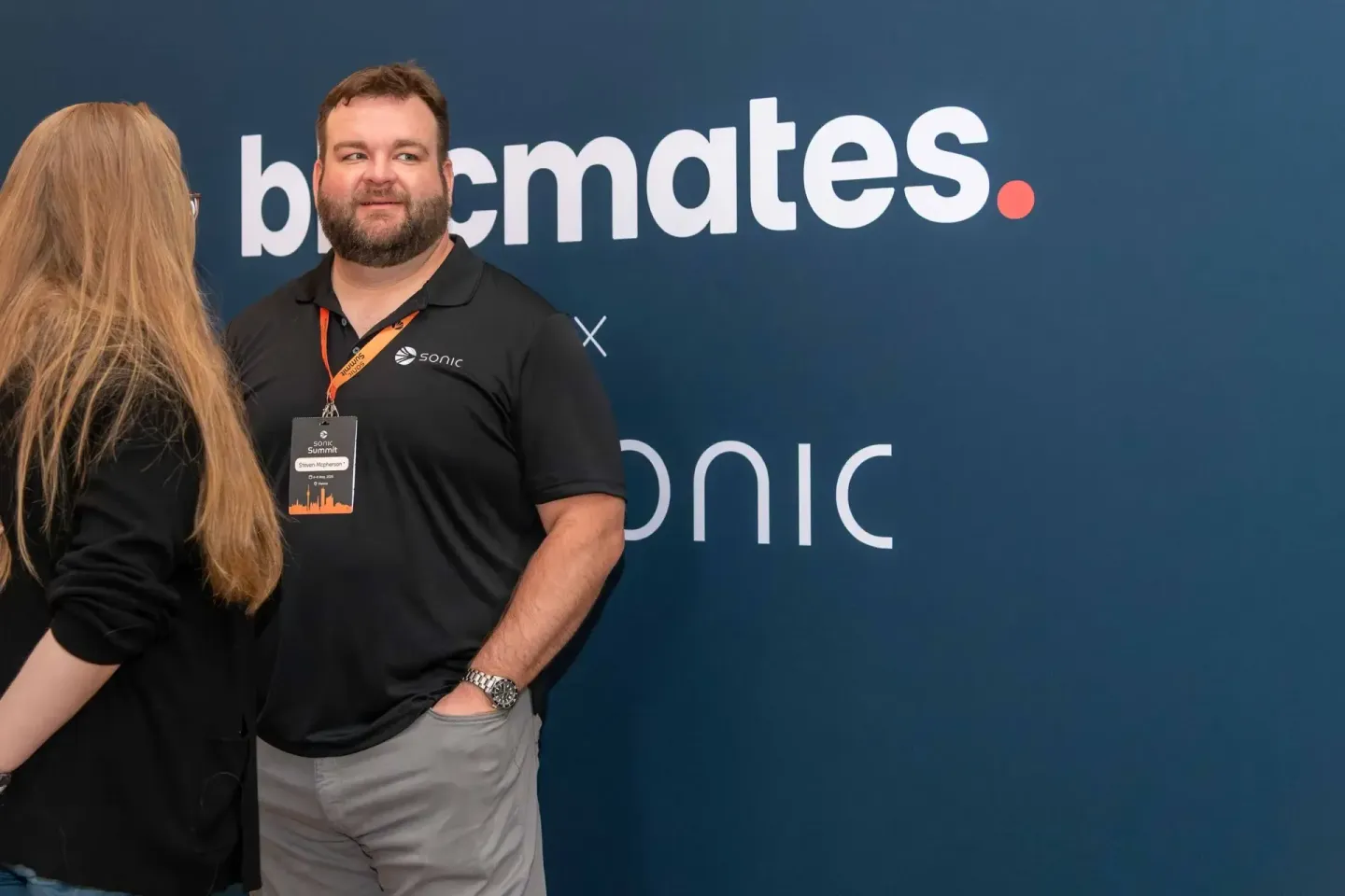 Eventfotograf dokumentiert Gespräch zwischen zwei Personen beim Sonic Summit vor blauer Kulisse mit Branding