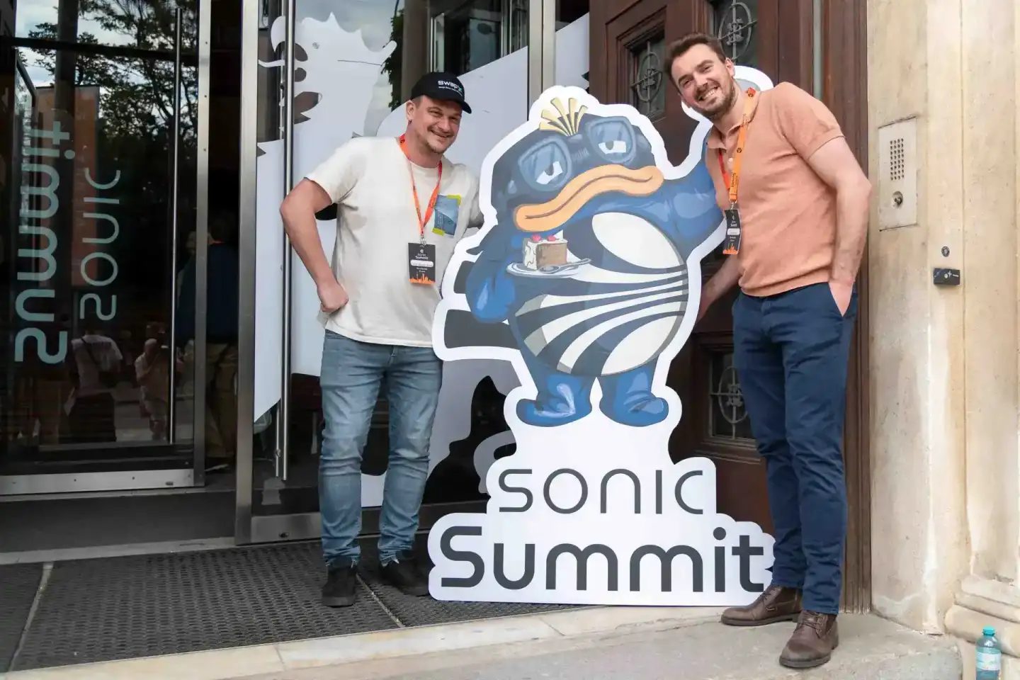 Zwei Männer posieren vor dem Sonic Summit Logo bei einem Firmenevent Wien, beide tragen Lanyards und lächeln in die Kamera