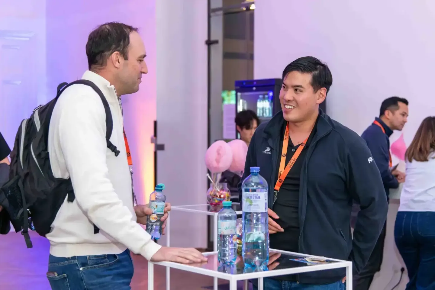 Zwei Männer im Gespräch beim Sonic Summit Event in Wien, mit Getränken und orangem Lanyards, im Hintergrund andere Gäste und 