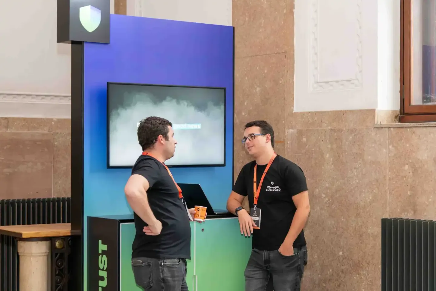 Zwei Männer in schwarzen T-Shirts mit Badges unterhalten sich vor einem interaktiven Display bei einem Firmenevent Wien