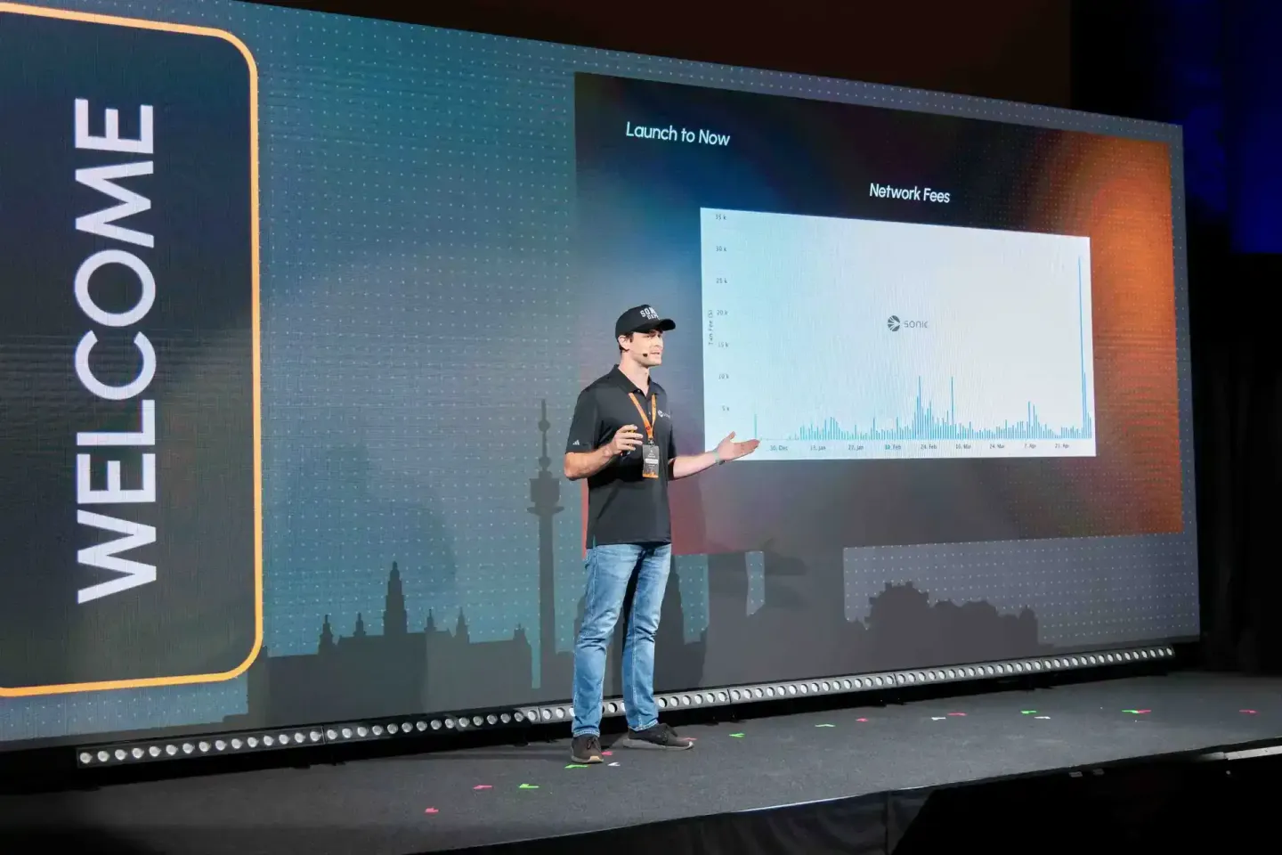 Sprecher präsentiert Netzwerk-Fee-Statistiken auf der Sonic Summit vor großem Screen mit Eventfotograf Wien