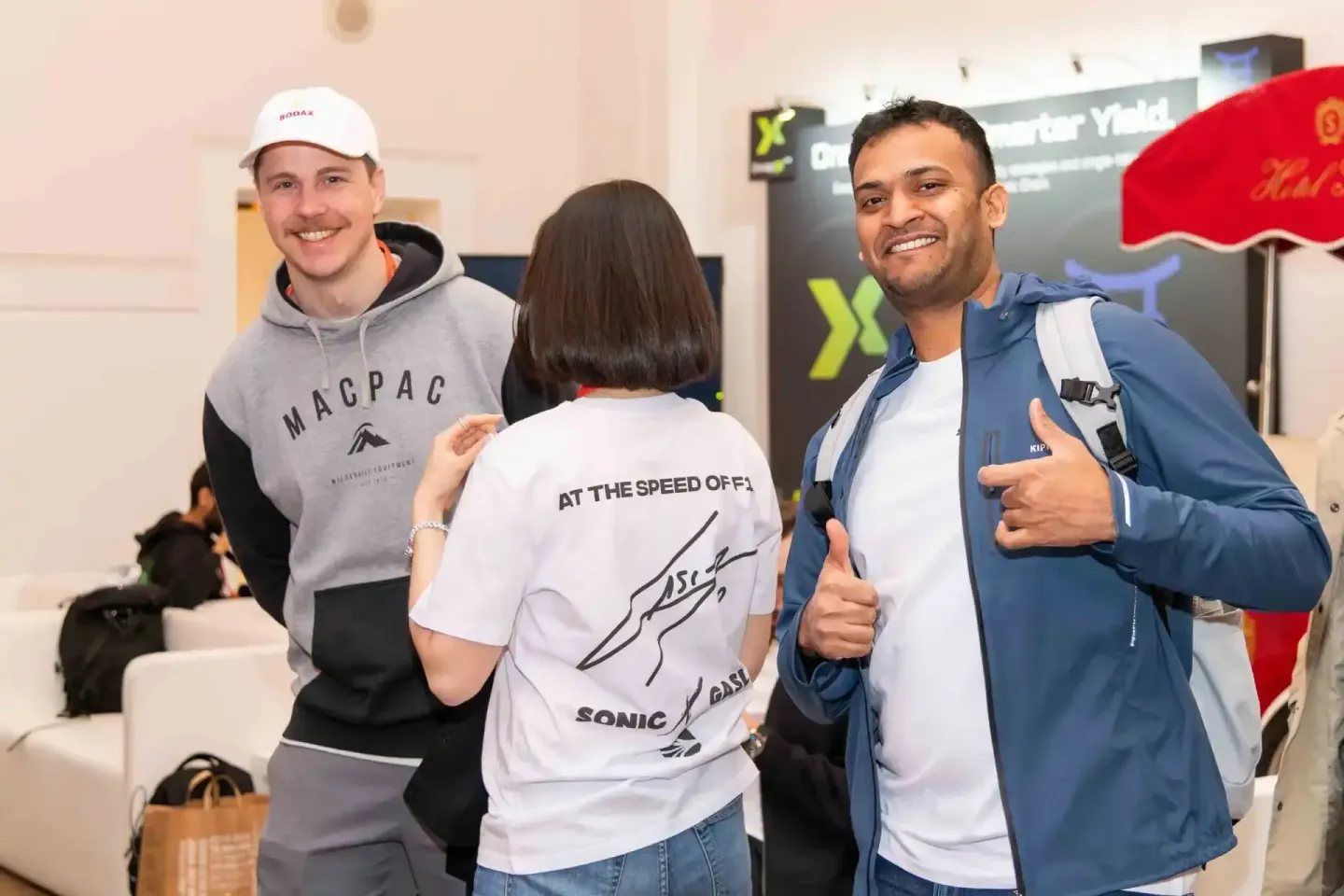 Drei Personen beim Sonic Summit Event in Wien - Mann mit Kappe und MACPAC-Hoodie, Frau in signiertem weißem Shirt, Mann in bl