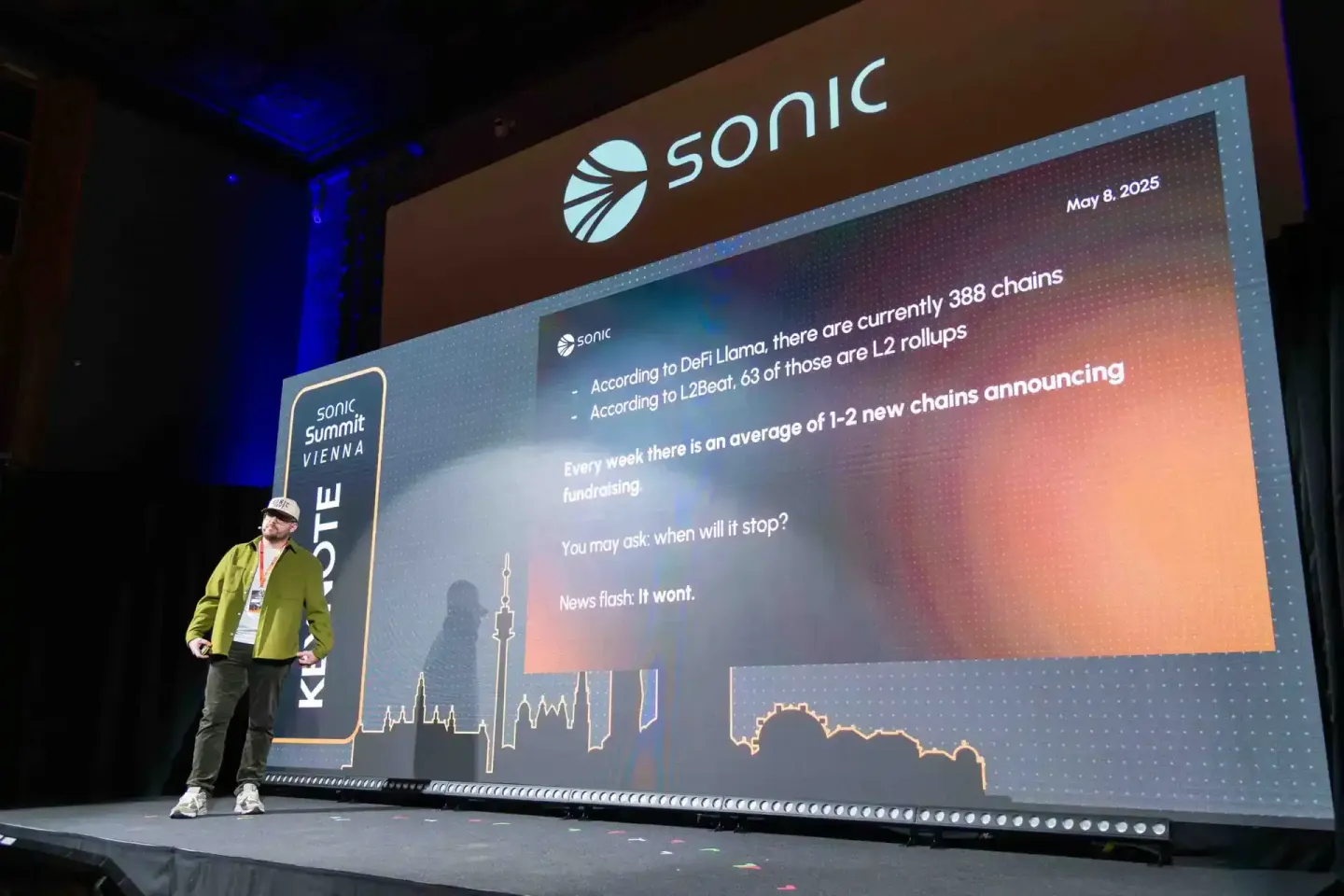 Eventfotograf präsentiert auf der Sonic Summit Vienna vor großem Screen mit DeFi und L2-Blockchain Daten