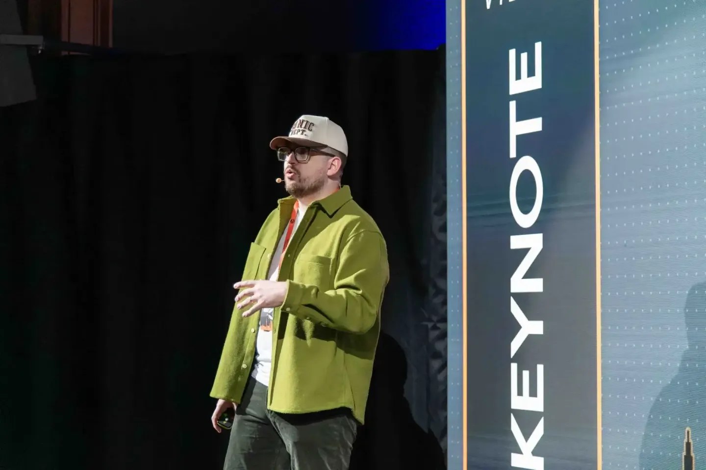 Sprecher in grünem Hemd und weißer Kappe präsentiert beim Sonic Summit Event auf der Bühne vor Publikum