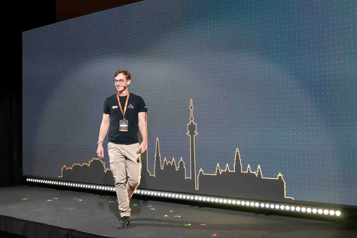 Sprecher auf der Sonic Summit Bühne in Wien, im Hintergrund eine goldene Skyline-Illustration, Eventfotografie Wien