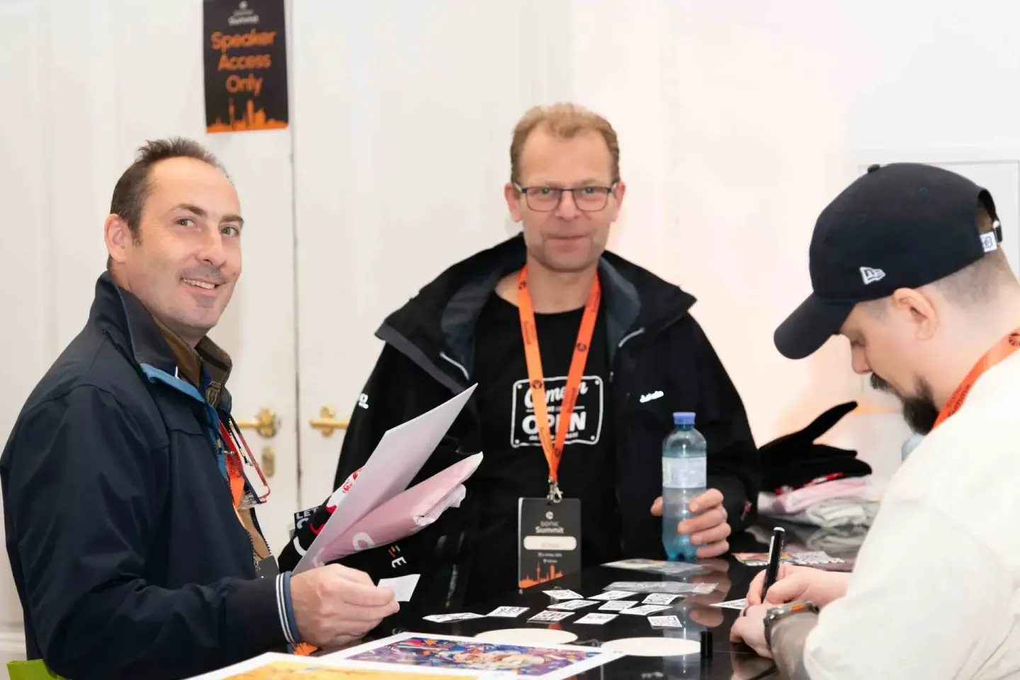 Drei Männer beim Sonic Summit Event in Wien diskutieren an einem Tisch. Ein Eventfotograf dokumentiert die Networking-Szene m