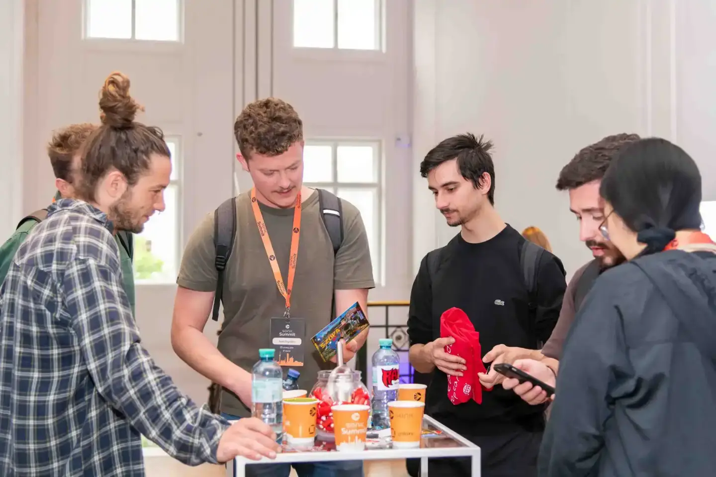 Fünf Personen beim Sonic Summit Event in Wien diskutieren an einem Tisch mit Merchandise und Getränken, professionelle Eventf
