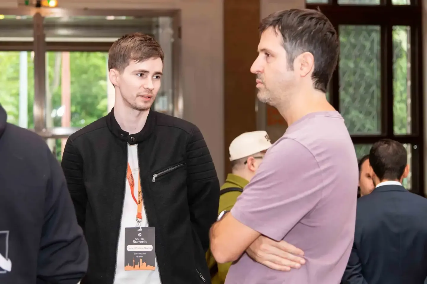 Zwei Männer im Gespräch beim Sonic Summit Event, einer trägt ein Eventfotograf-Badge, moderner Veranstaltungsort in Wien