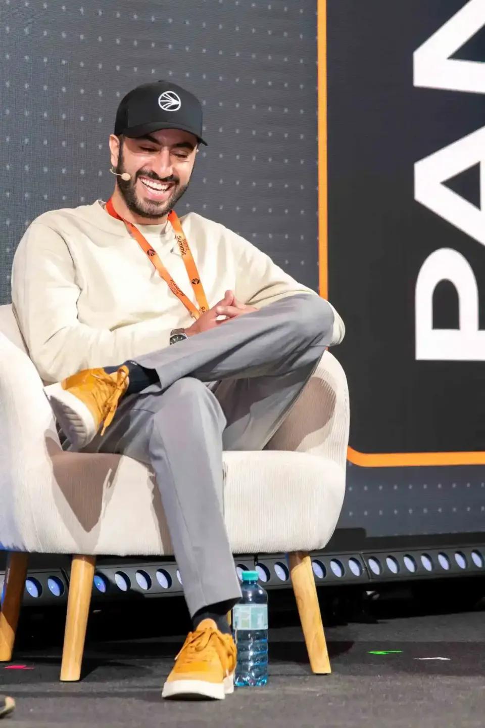 Lachender Mann mit schwarzer Kappe sitzt in weißem Sessel auf der Bühne des Sonic Summit Events, unser Eventfotograf Wien dok