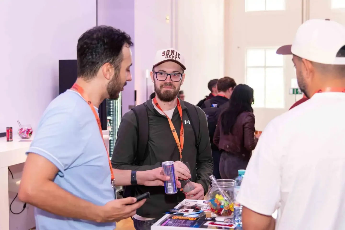 Drei Personen mit Lanyards beim Sonic Summit Firmenevent Wien, zwei unterhalten sich mit Getränken an einem Stehtisch