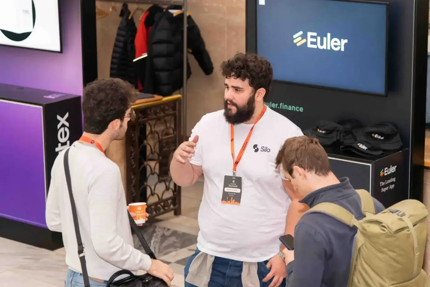 Eventfotograf dokumentiert Gespräch zwischen drei Personen auf der Sonic Summit in Wien, im Hintergrund Euler-Banner und Auss