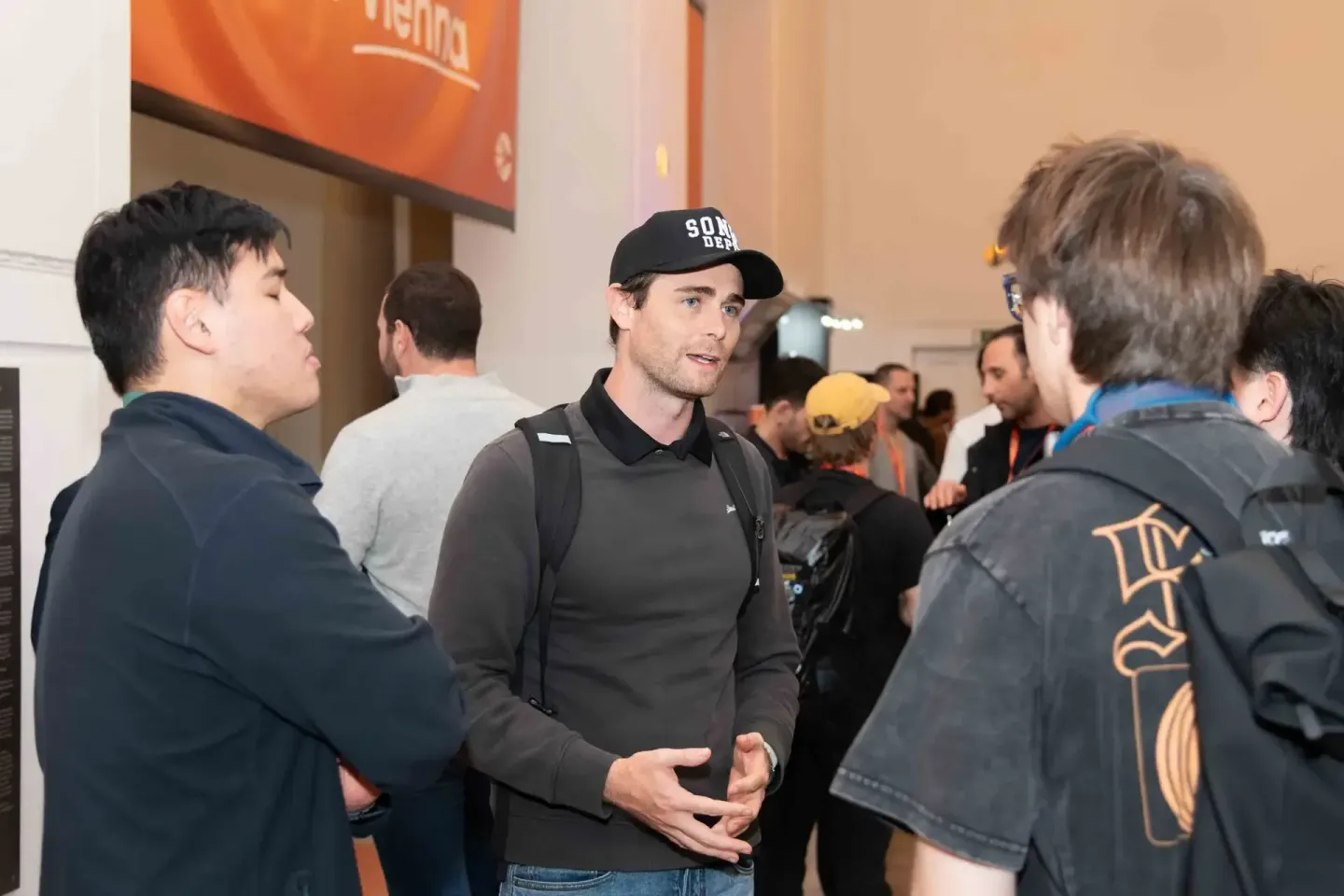 Eventfotograf dokumentiert Networking-Moment beim Sonic Summit: Mann mit schwarzer Kappe im Gespräch mit mehreren Besuchern i