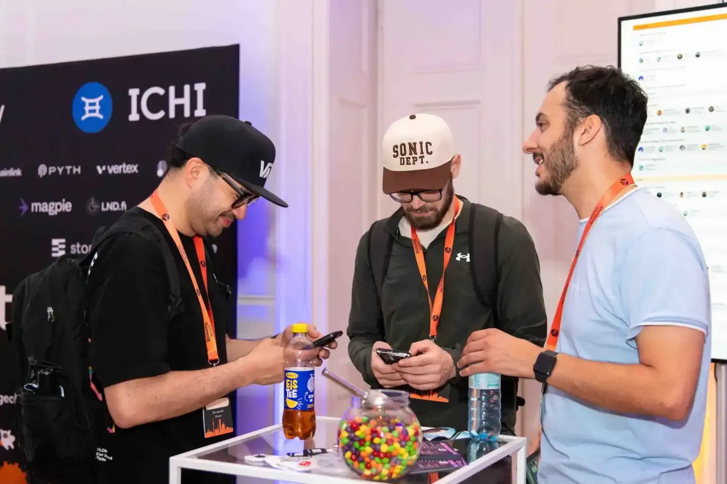 Drei Männer mit Lanyards beim Networking auf der Sonic Summit Konferenz mit ICHI-Logos im Hintergrund – Eventfotografie Wien