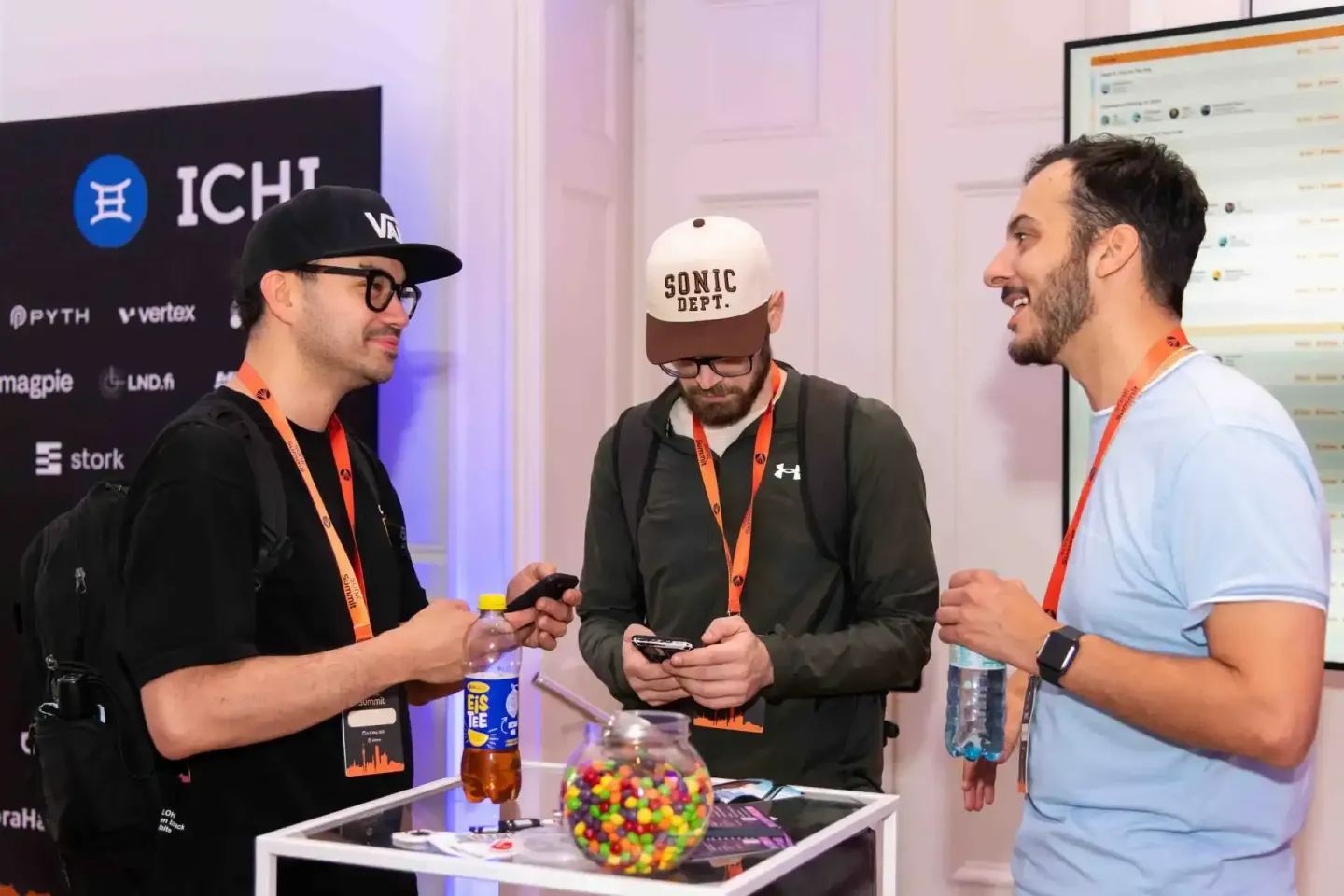 Drei Männer im Gespräch bei einem Firmenevent Wien, einer trägt eine Sonic Dept. Kappe, alle tragen orange Lanyards