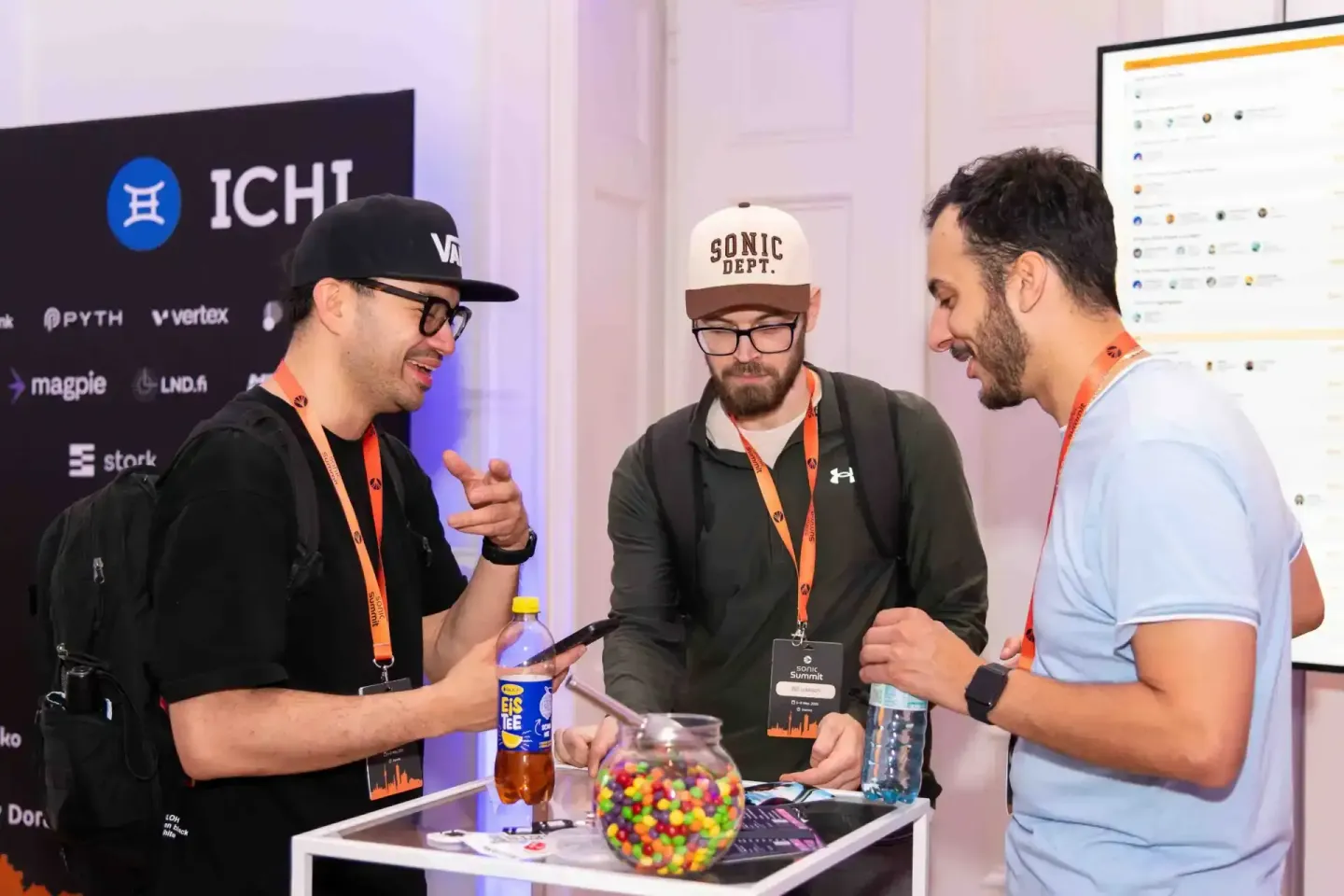 Drei Teilnehmer beim Sonic Summit Event in Wien im Gespräch an einem Stehtisch mit Getränken und Süßigkeiten, Eventfotograf d