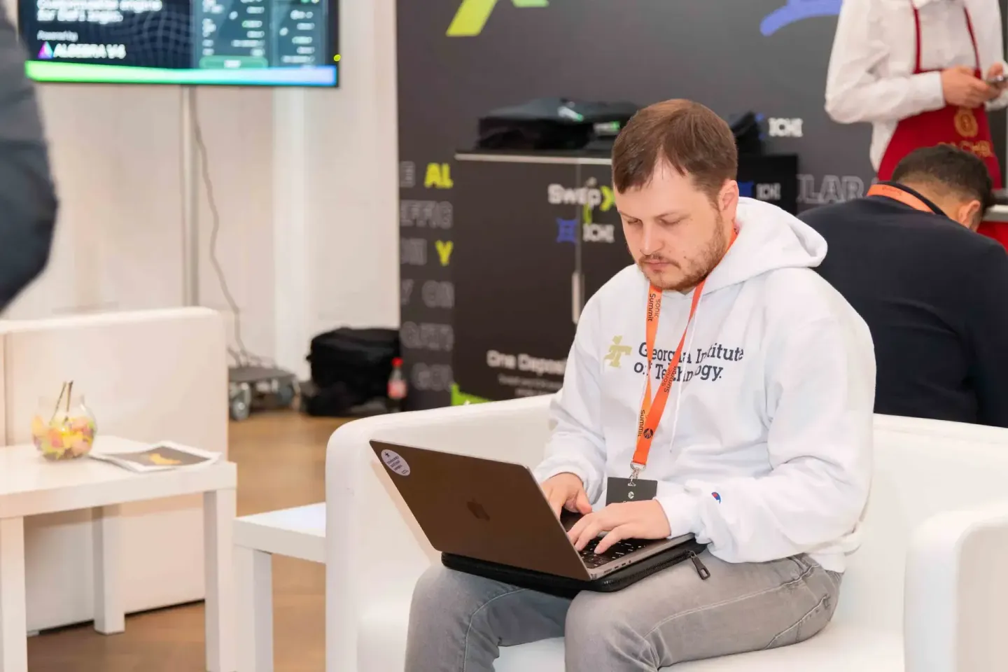 Teilnehmer beim Sonic Summit arbeitet konzentriert am Laptop, trägt Eventpass – Eventfotografie Wien