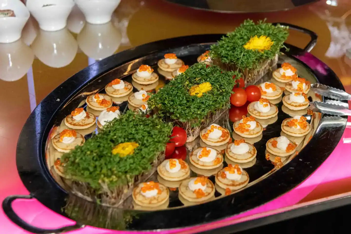 Elegante Appetizer-Platte mit Blini, Kaviar und Creme auf schwarzem Tablett, dekoriert mit frischen Kräutern und Tomaten – pr