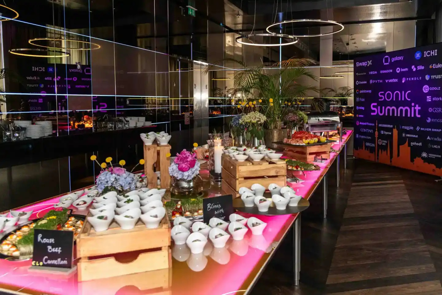 Elegante Catering-Tafel mit weißen Schälchen, Blumenarrangements und pinker LED-Beleuchtung beim Sonic Summit Event – profess