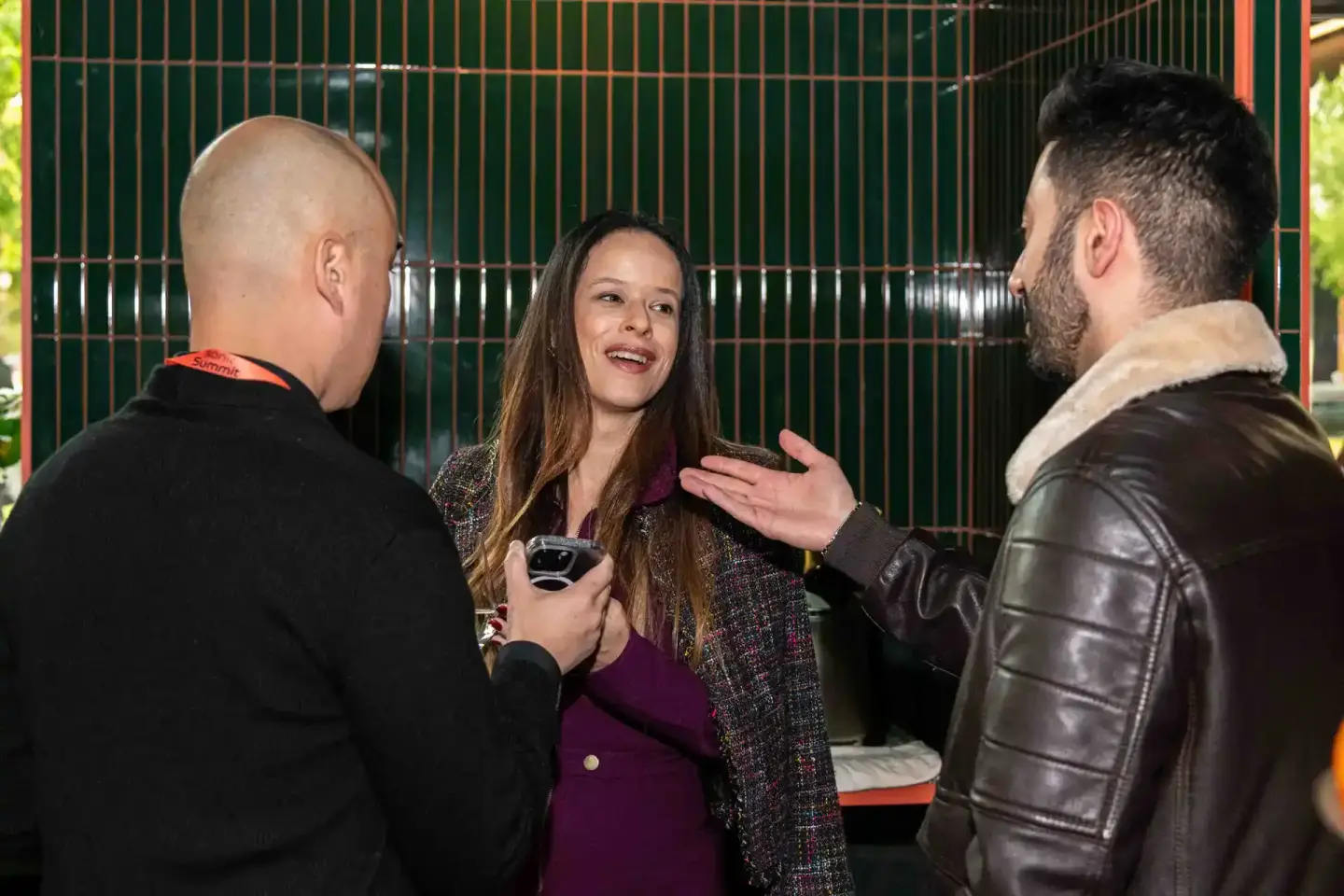 Drei Personen im angeregten Gespräch vor grüner Metallwand beim Sonic Summit Event – professionelle Eventfotografie Wien