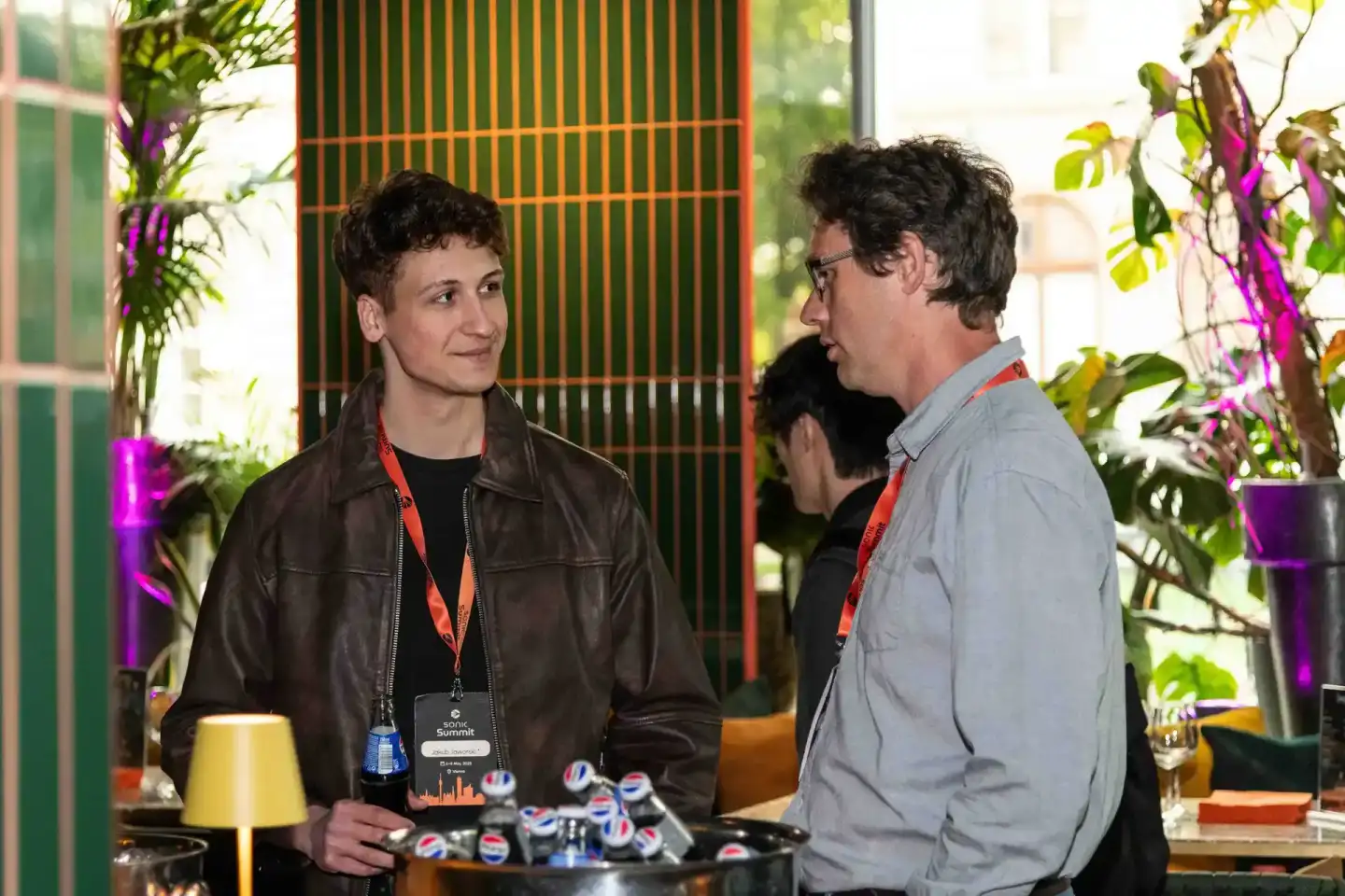 Zwei Besucher im Gespräch beim Sonic Summit Event in Wien, umgeben von grünen Pflanzen und moderner Dekoration