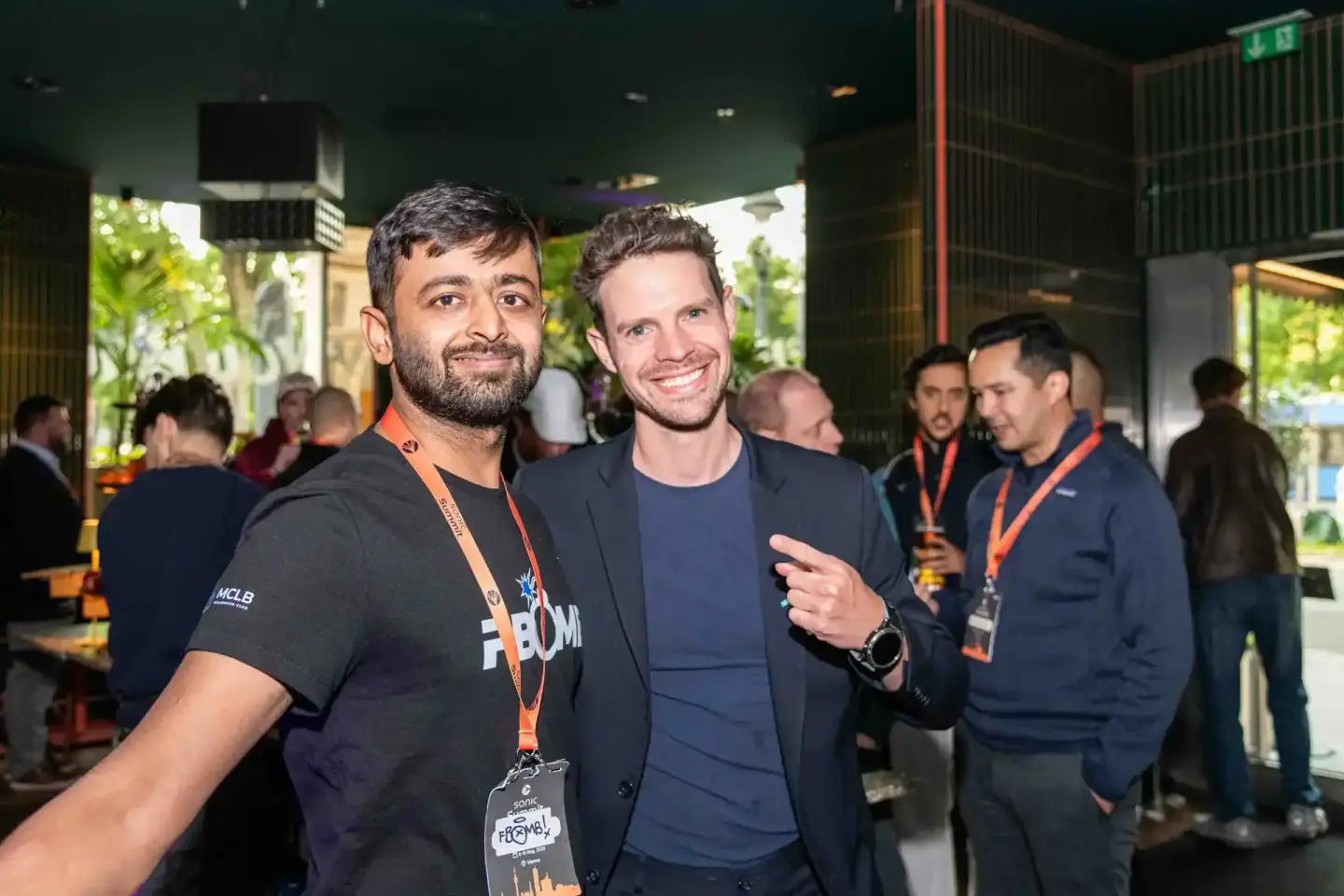 Zwei Männer bei einem Firmenevent in Wien, einer trägt ein schwarzes Eventfotograf-Shirt mit Lanyard, beide lächeln in die Ka
