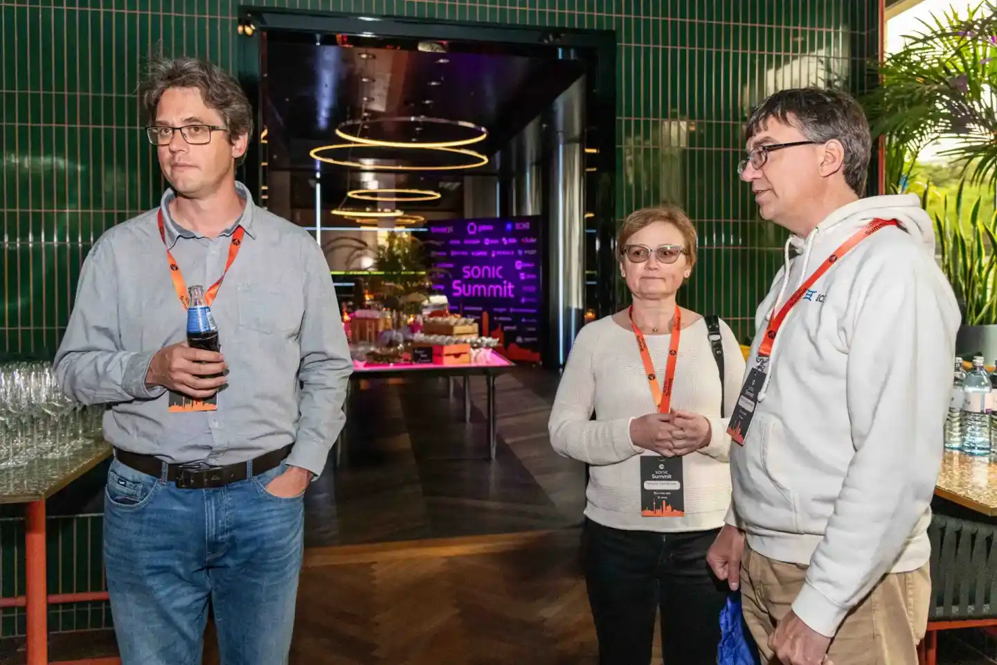 Drei Personen mit Konferenz-Badges beim sonic-summit Event in Wien, im Hintergrund grüne Wandverkleidung und beleuchteter Ein