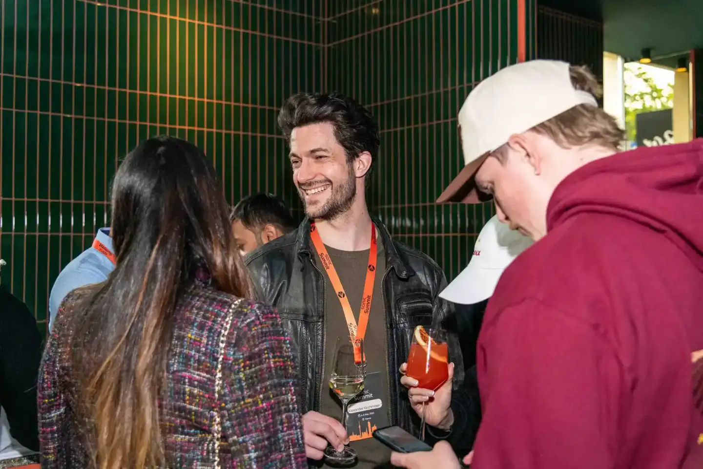 Eventfotograf dokumentiert lebhafte Networking-Szene beim Sonic Summit mit Gästen in eleganter Atmosphäre vor grüner Wand