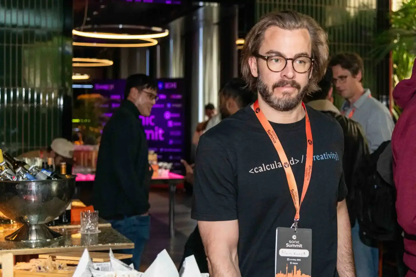 Teilnehmer beim Sonic Summit Wien trägt schwarzes T-Shirt mit Aufdruck und Besucherausweis, im Hintergrund Eventlocation mit 