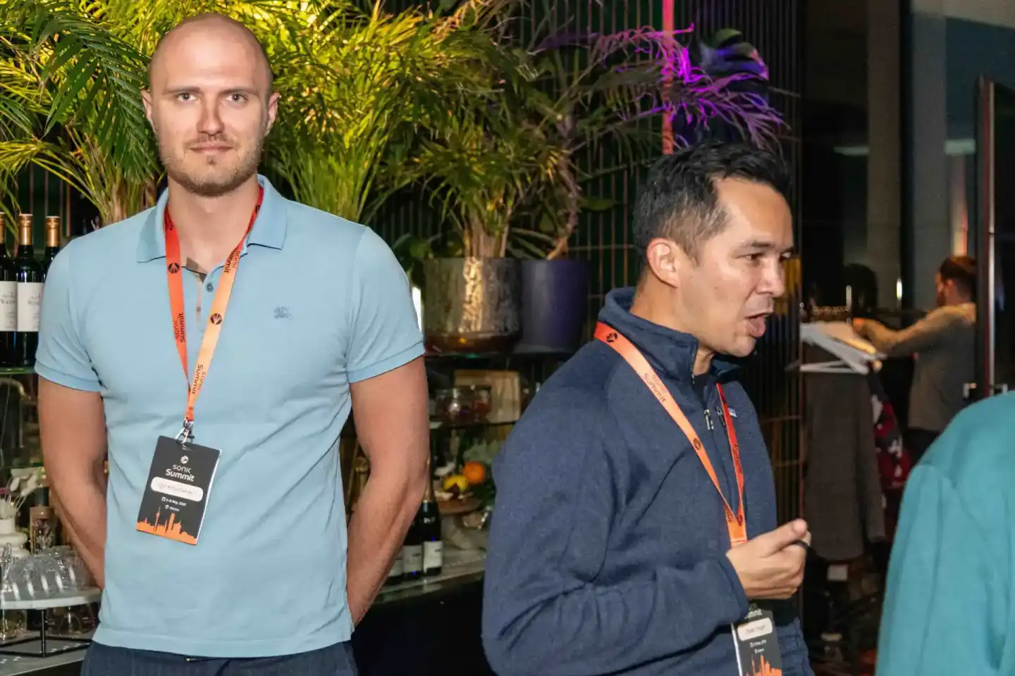 Zwei Männer mit Event-Badges beim Sonic Summit in Wien, im Hintergrund grüne Pflanzen und moderne Bar-Einrichtung