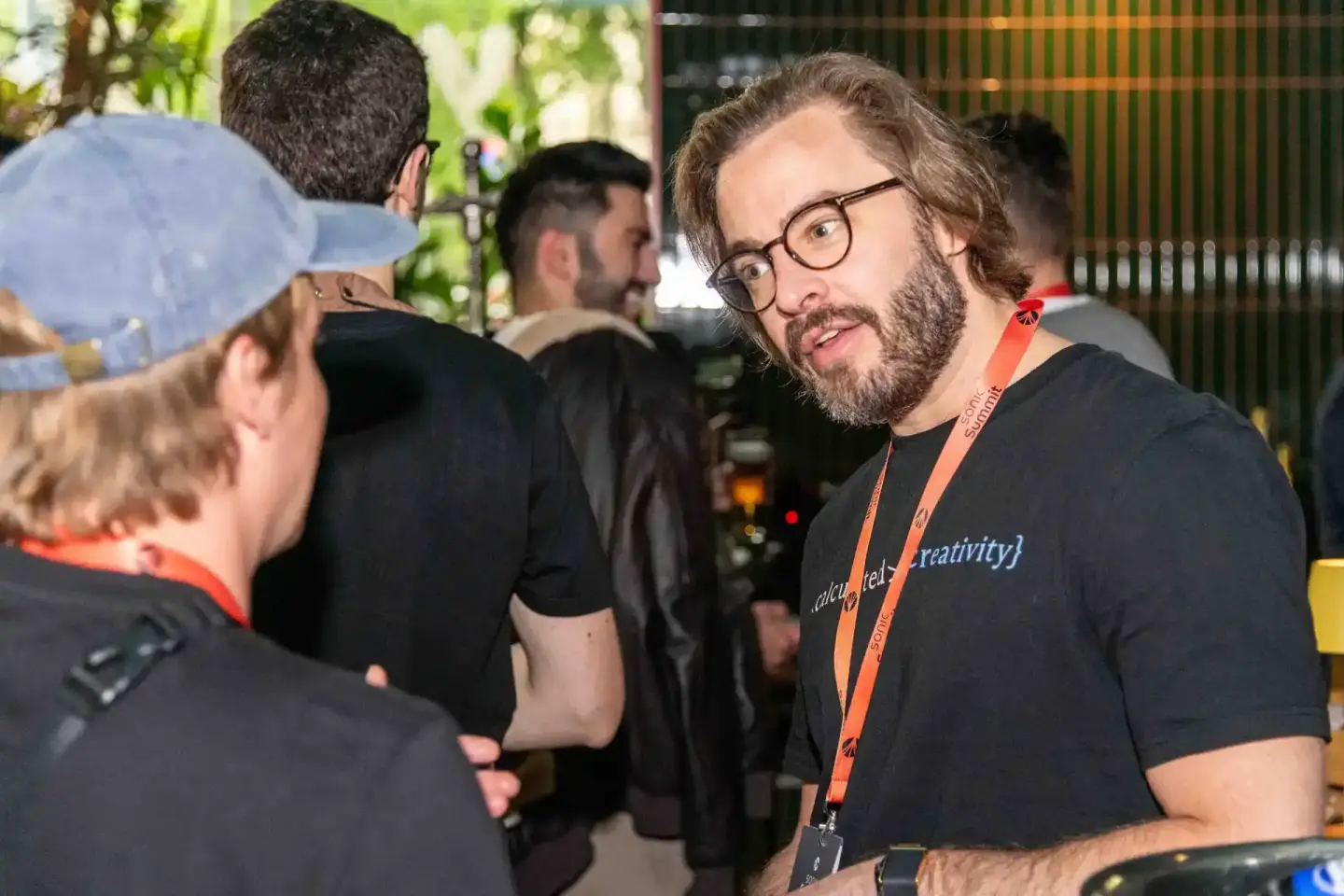 Eventfotograf dokumentiert Gespräch zwischen zwei Besuchern beim Sonic Summit in Wien, Mann mit Brille und Bart trägt orange 