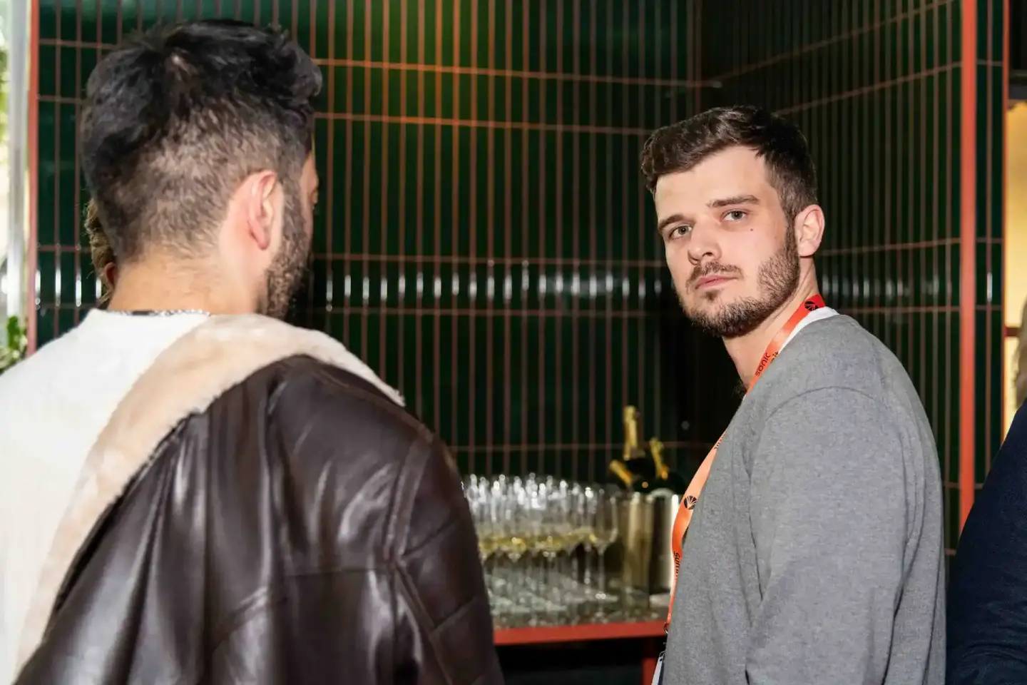 Zwei Männer im Gespräch bei einem Firmenevent in Wien vor grüner Wand mit Bar im Hintergrund