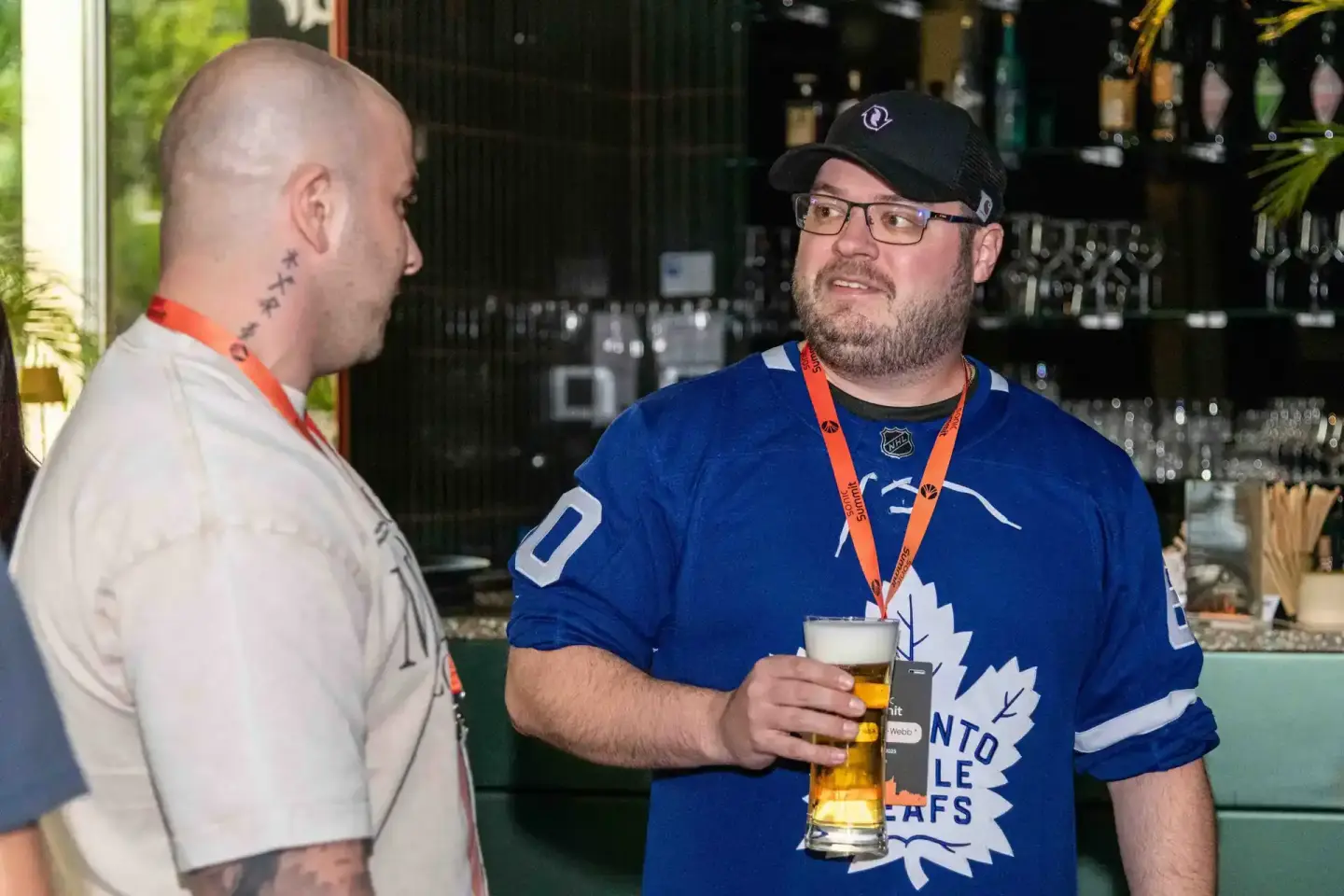 Zwei Männer im Gespräch bei einem Firmenevent in Wien, einer trägt ein Toronto Maple Leafs Trikot und hält ein Bier