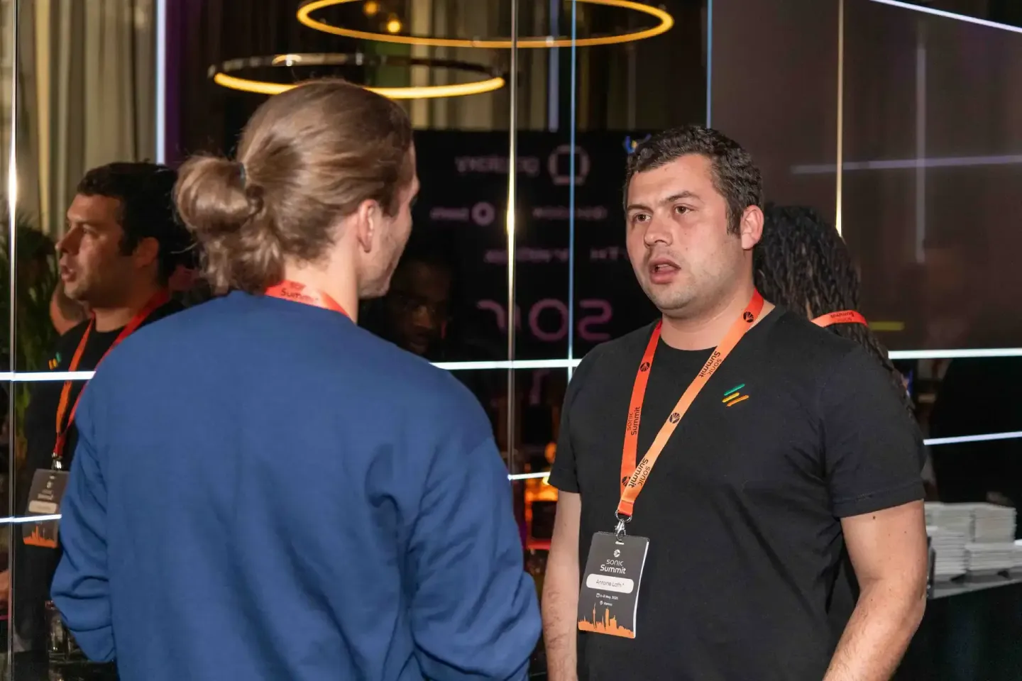 Zwei Personen im Gespräch beim Sonic Summit Event in Wien, beide tragen Lanyards, modernes Event-Setting mit LED-Beleuchtung