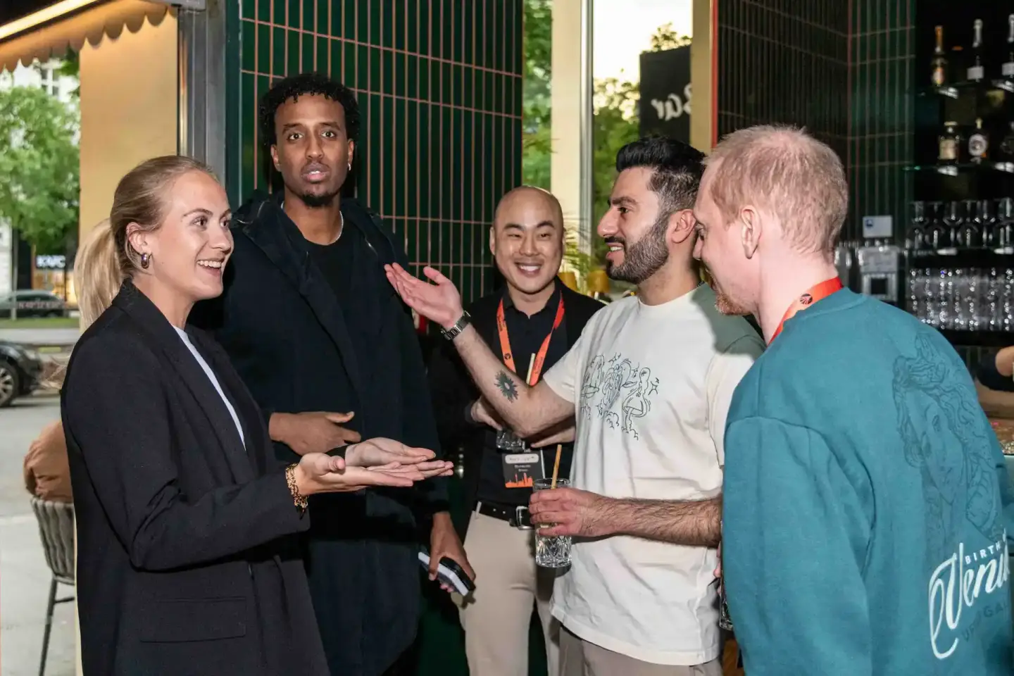 Gruppe von fünf Personen im lockeren Gespräch bei einem Firmenevent Wien, moderne Lounge-Atmosphäre mit grünem Gitter im Hint