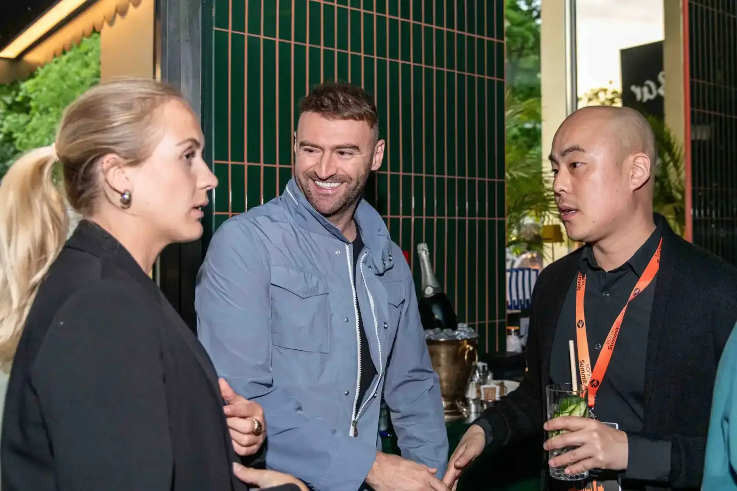 Drei Personen im Gespräch bei einem Firmenevent Wien, Mann in blauem Hemd lächelt, Frau in schwarzer Jacke und Mann mit orang