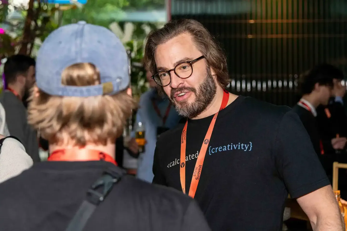 Eventfotograf dokumentiert Gespräch zwischen zwei Besuchern beim Sonic Summit in Wien, Mann mit Brille und Bart trägt Nametag