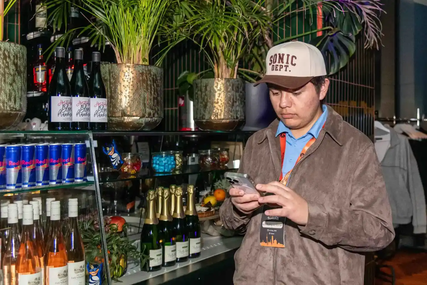 Besucher beim Sonic Summit Event in Wien nutzt sein Smartphone vor einer Bar mit Getränkeauswahl