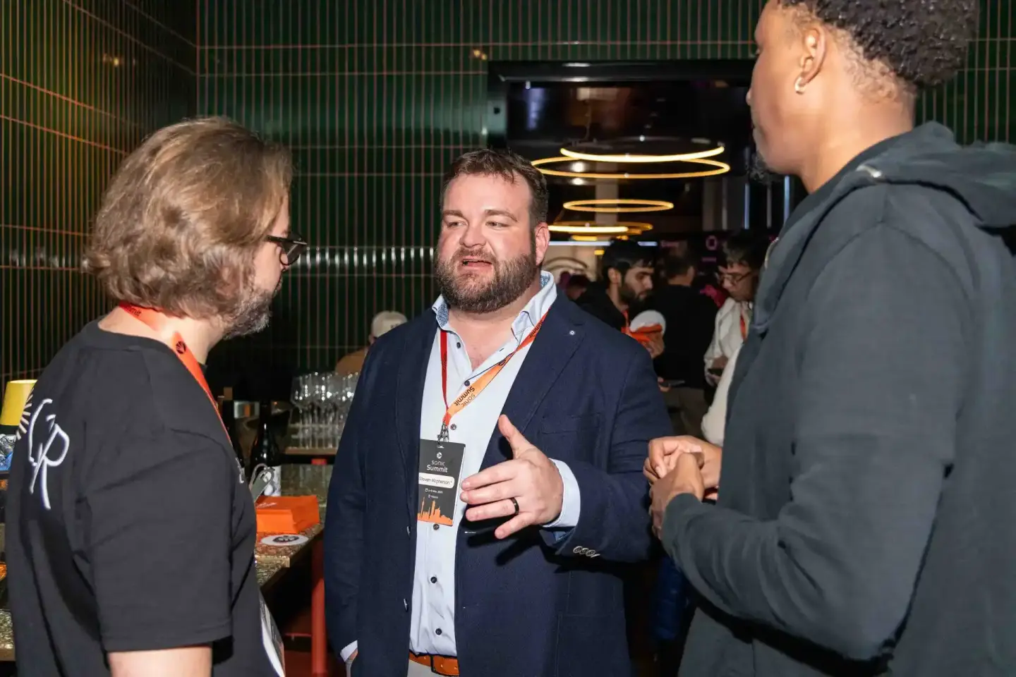 Drei Personen im Gespräch bei der Sonic Summit in Wien, Eventfotografie mit modernem grünem Hintergrund und goldenen Lichtele