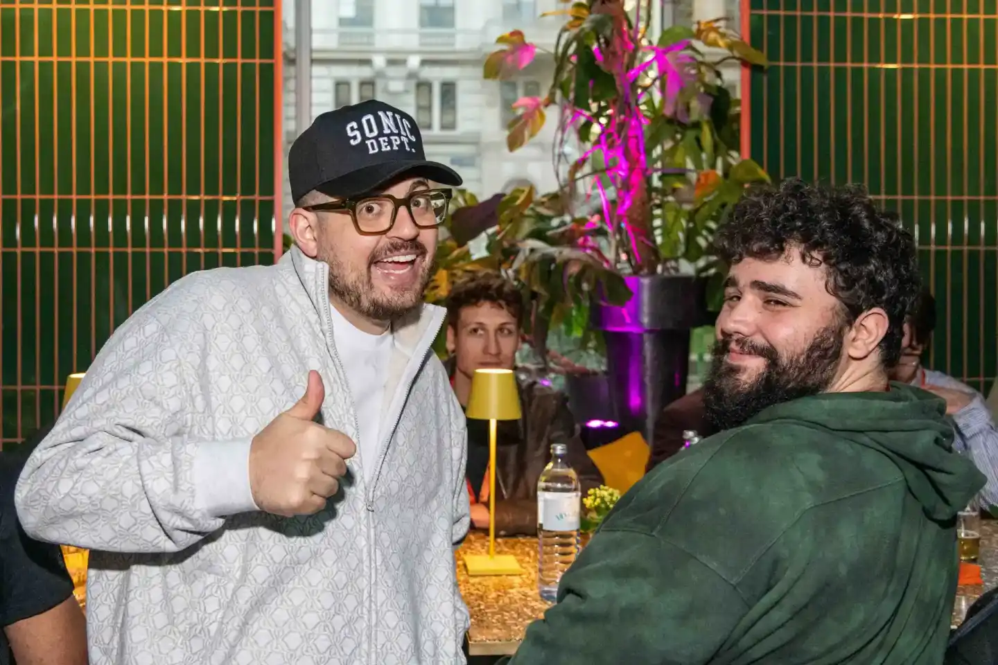 Zwei Männer im Gespräch bei einem Firmenevent Wien, einer trägt eine schwarze Cap und Brille, im Hintergrund magenta blühende