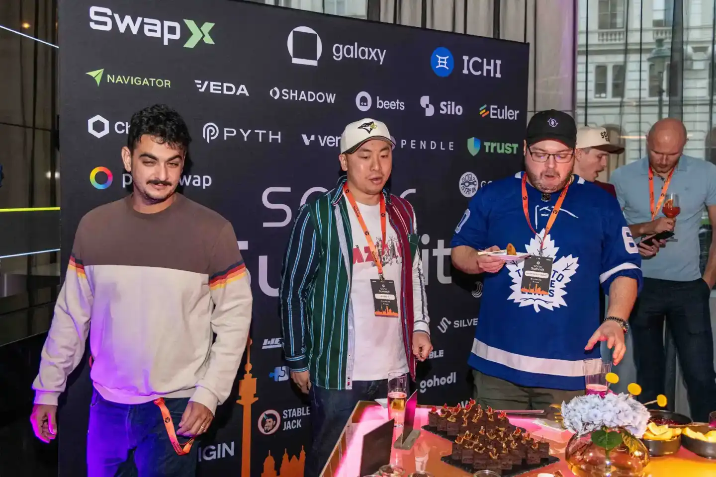 Vier Männer bei einem Sonic Summit Event vor einer Sponsor-Wand mit Kryptowährungs-Logos, einer trägt ein Toronto Maple Leafs